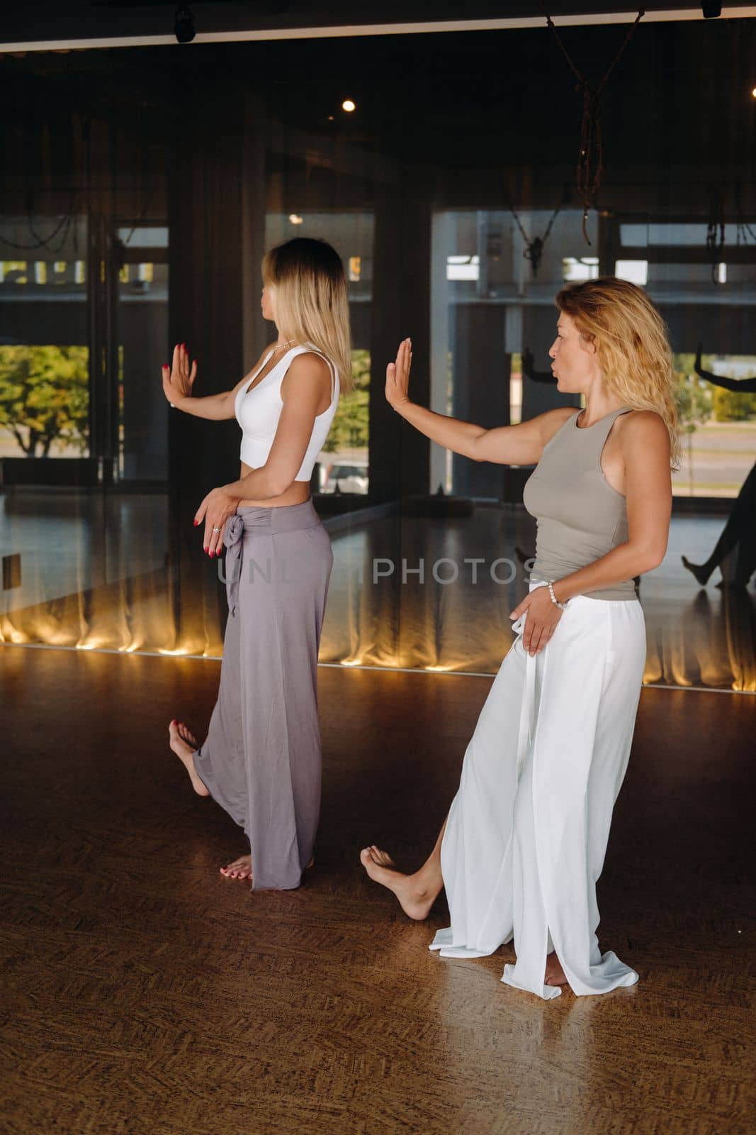 Two beautiful women are doing yoga standing up in the fitness room by Lobachad