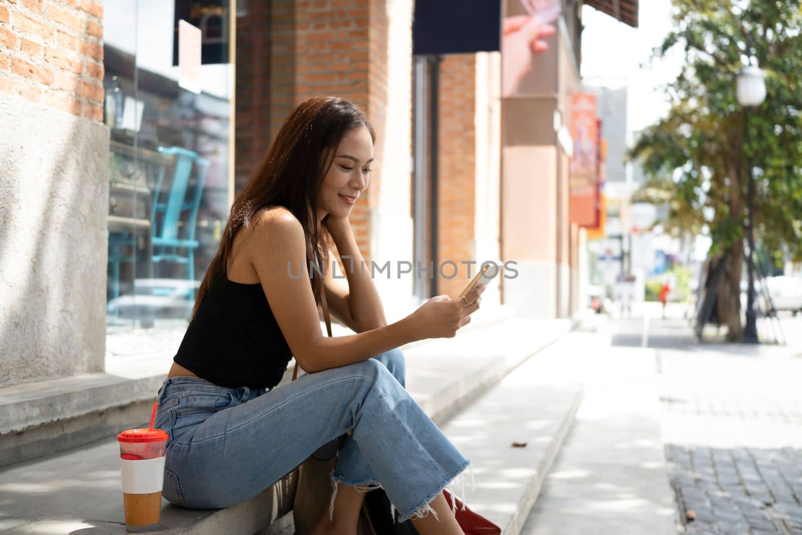 Smiling Asian woman sitting on stairs using smart phone. by prathanchorruangsak