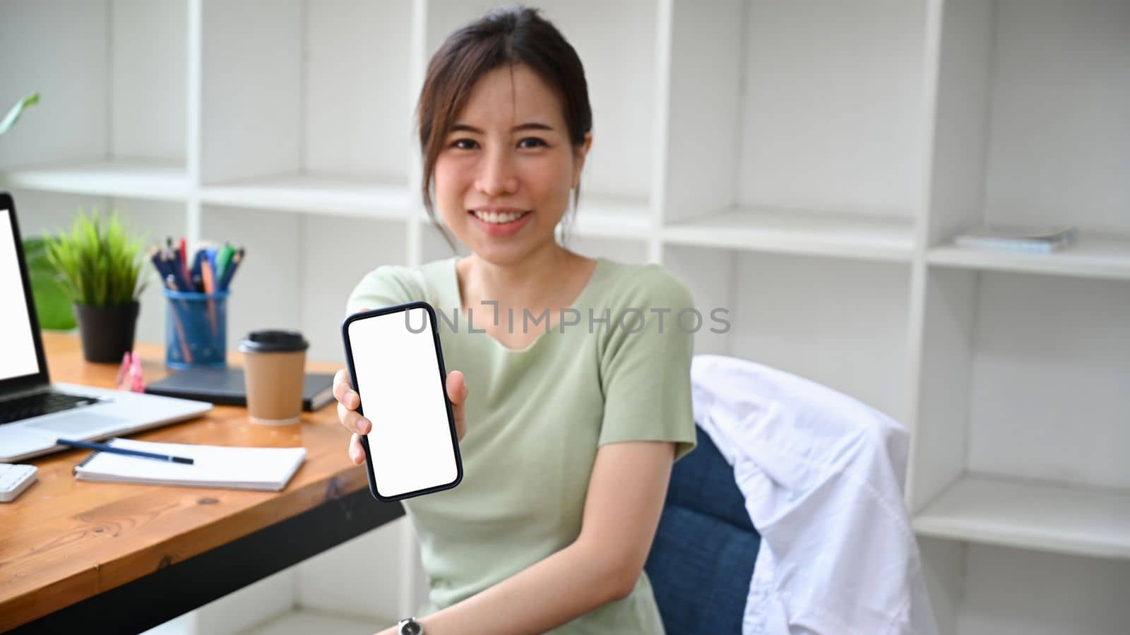 Smiling Asian woman holding and showing smart phone with blank screen. by prathanchorruangsak