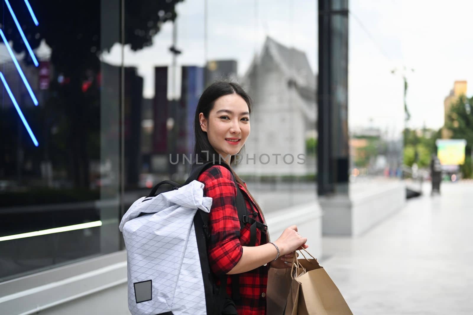 Smiling young Asian woman holding shopping bags and walking at outdoor shopping mall. by prathanchorruangsak