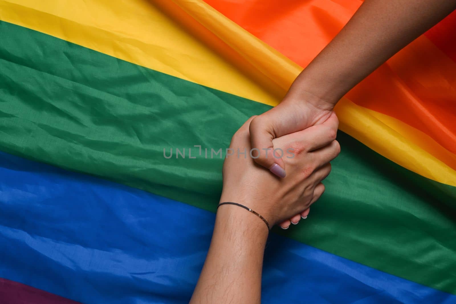 Two young women lesbian couple holding hands over LGBT pride flag. by prathanchorruangsak