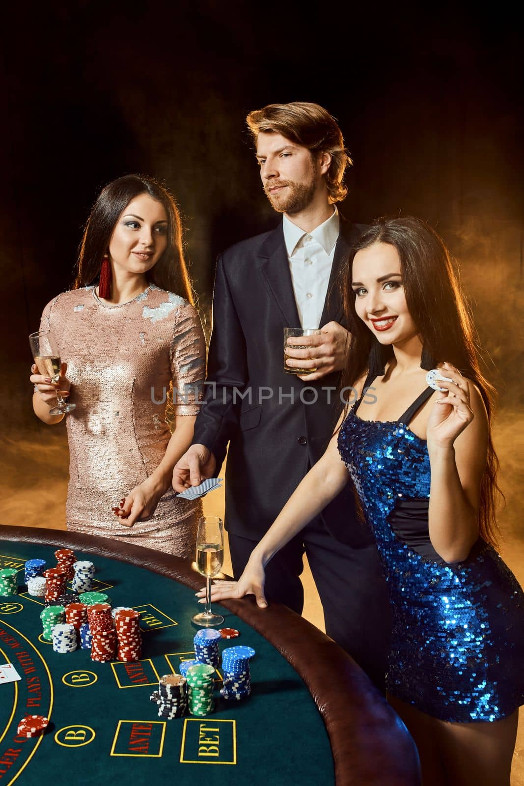 Two beautiful women and young man play on poker table in casino, focus on man and brunette by nazarovsergey