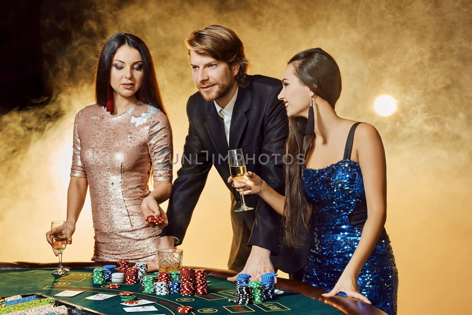 Two beautiful women and young man play on poker table in casino, focus on man and brunette by nazarovsergey