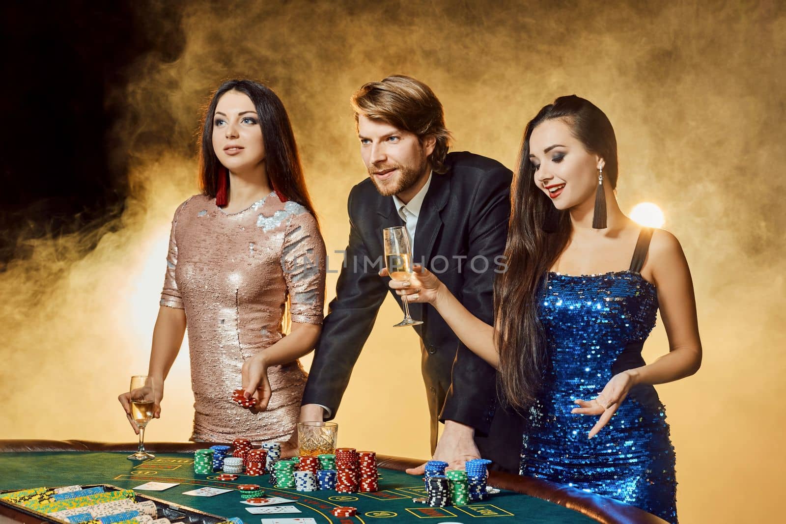 Two beautiful women and young man play on poker table in casino, focus on man and brunette by nazarovsergey