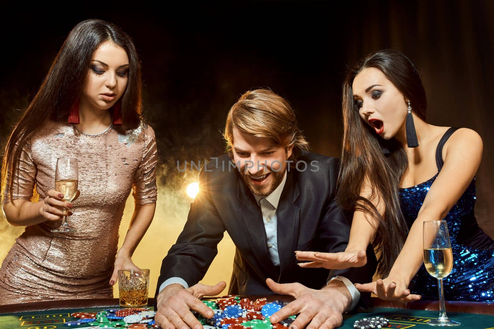 Two beautiful women and young man play on poker table in casino, focus on man and brunette by nazarovsergey