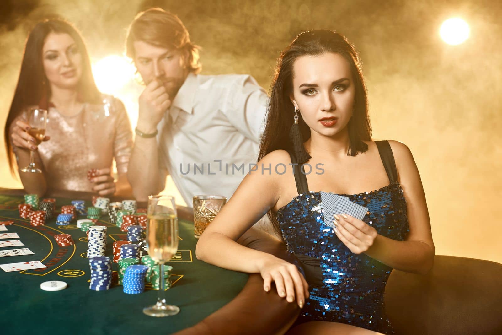 Group of an elegant people playing poker at the gambling house. Focus on a emotional brunette in a blue shiny dress by nazarovsergey