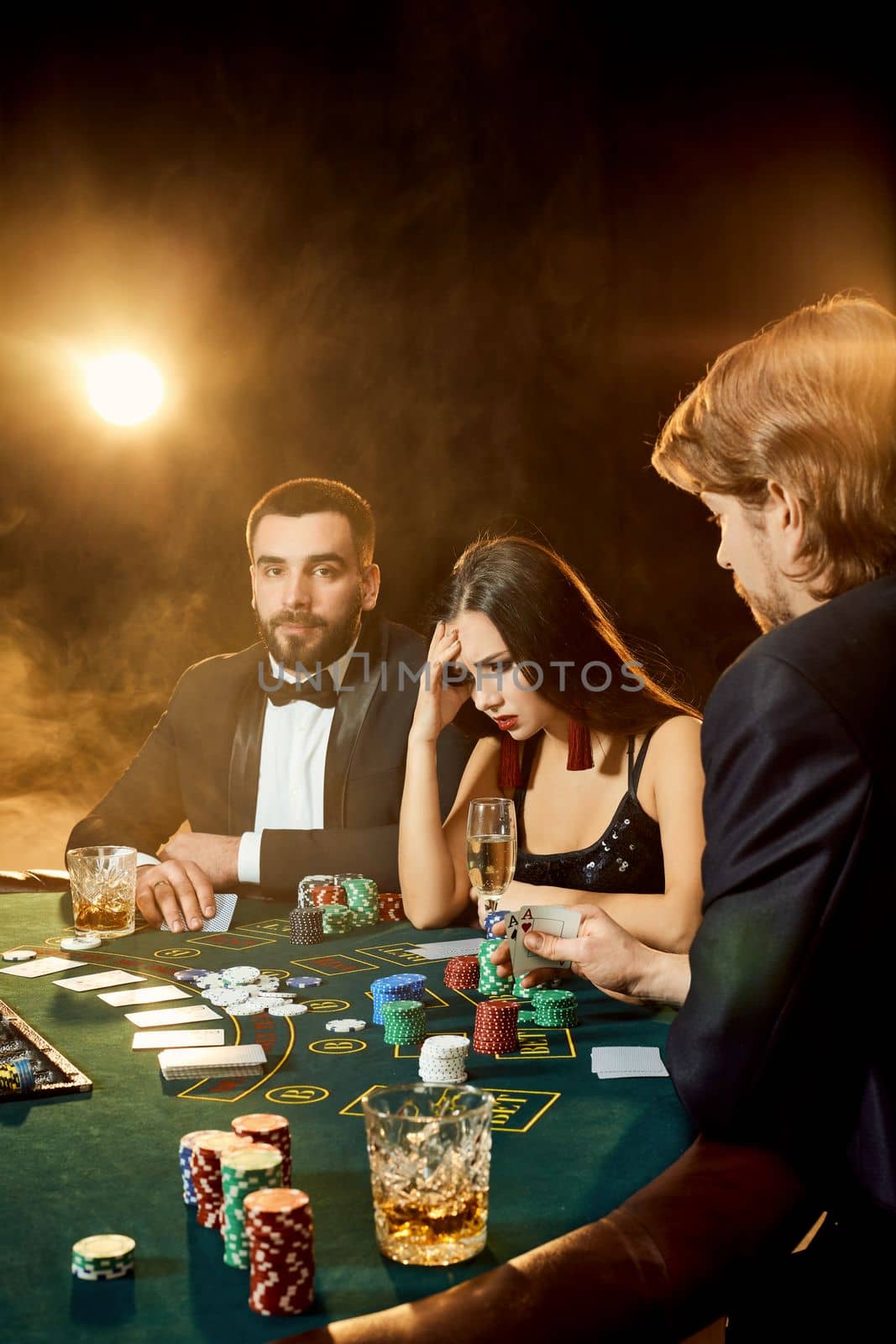 Group of young rich people is playing poker in the casino. Two men in business suits and a young woman in a black dress. Smoke. Casino. Poker
