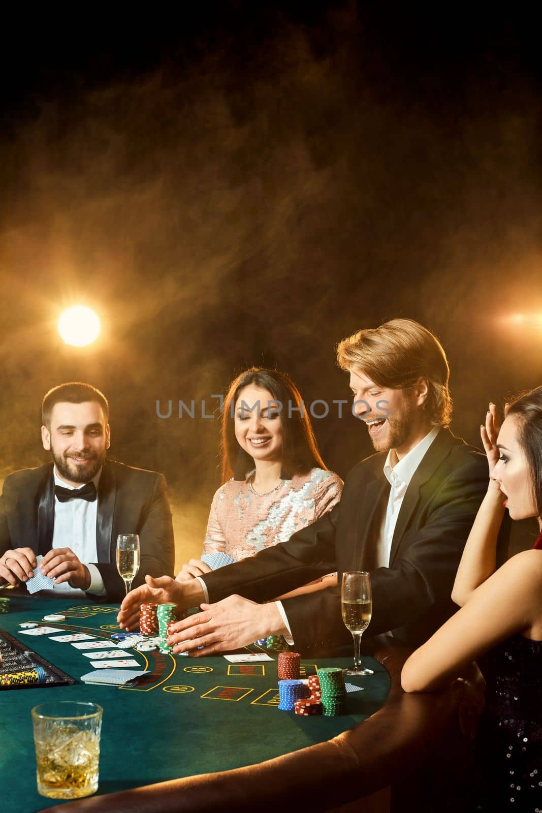 Upper class friends gambling in a casino. Two men in suits and two young women in dresses. Smoke. Casino. Poker
