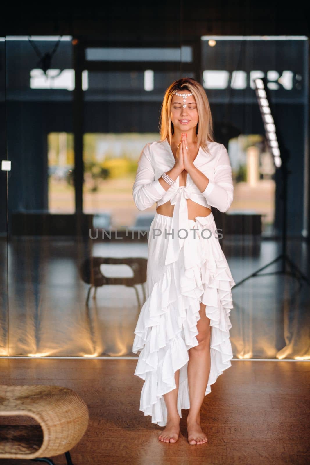 Portrait of a smiling girl in a white dress with her palms clasped in front of her.