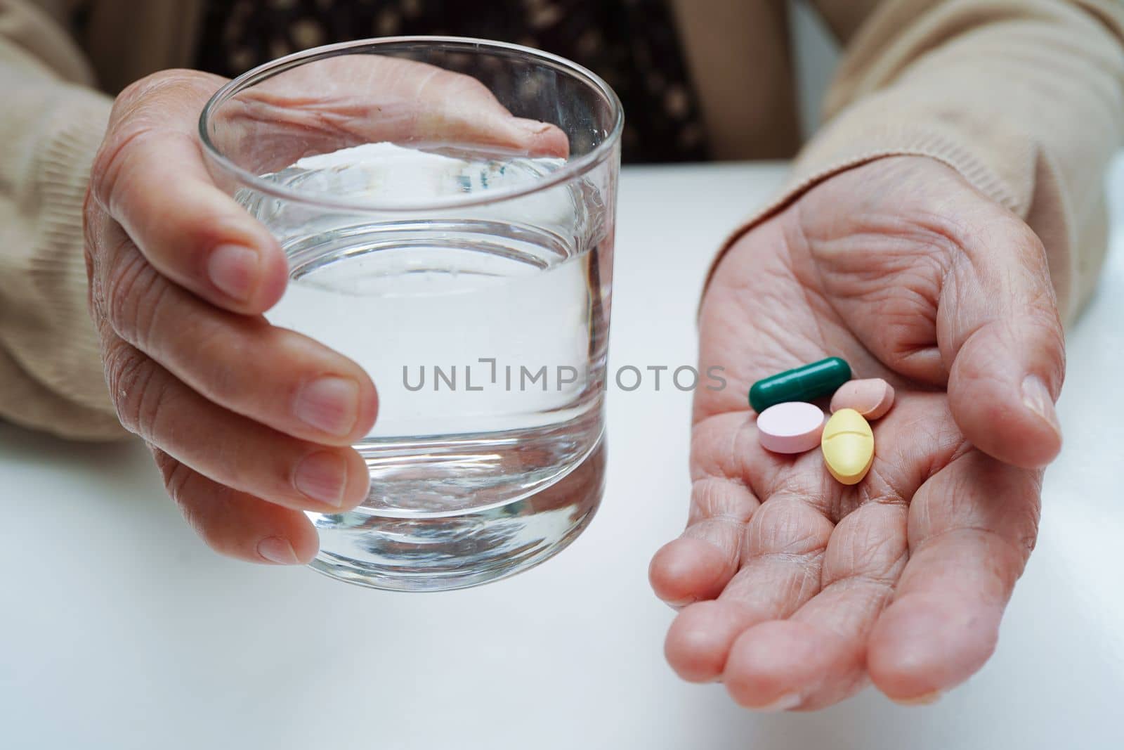 Asian elderly woman holding pill drug with water in glass, strong healthy medical concept. 