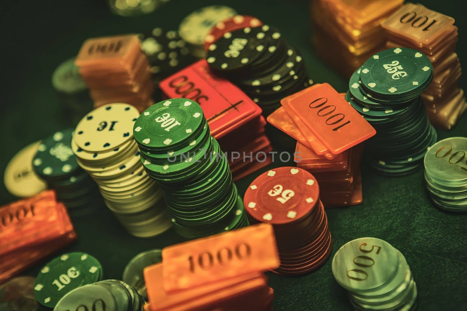 Poker chips are stacked neatly on a green textured table, the focus is on the chips with a shallow depth of field. The background is hazy with the smoke of cigars filling the room.