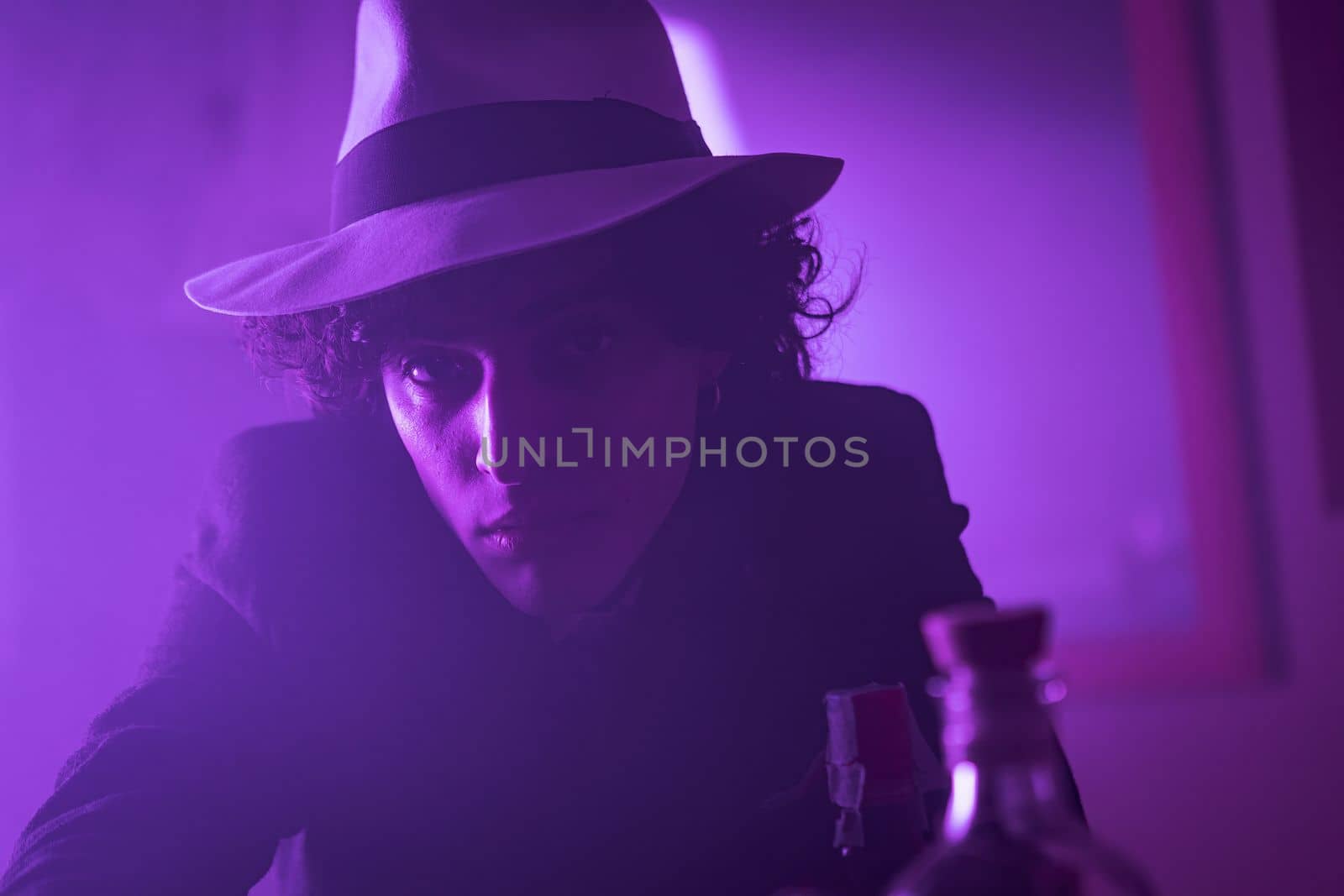 Young curly haired brunette man with hat and suit looks at the camera and smiles by pippocarlot