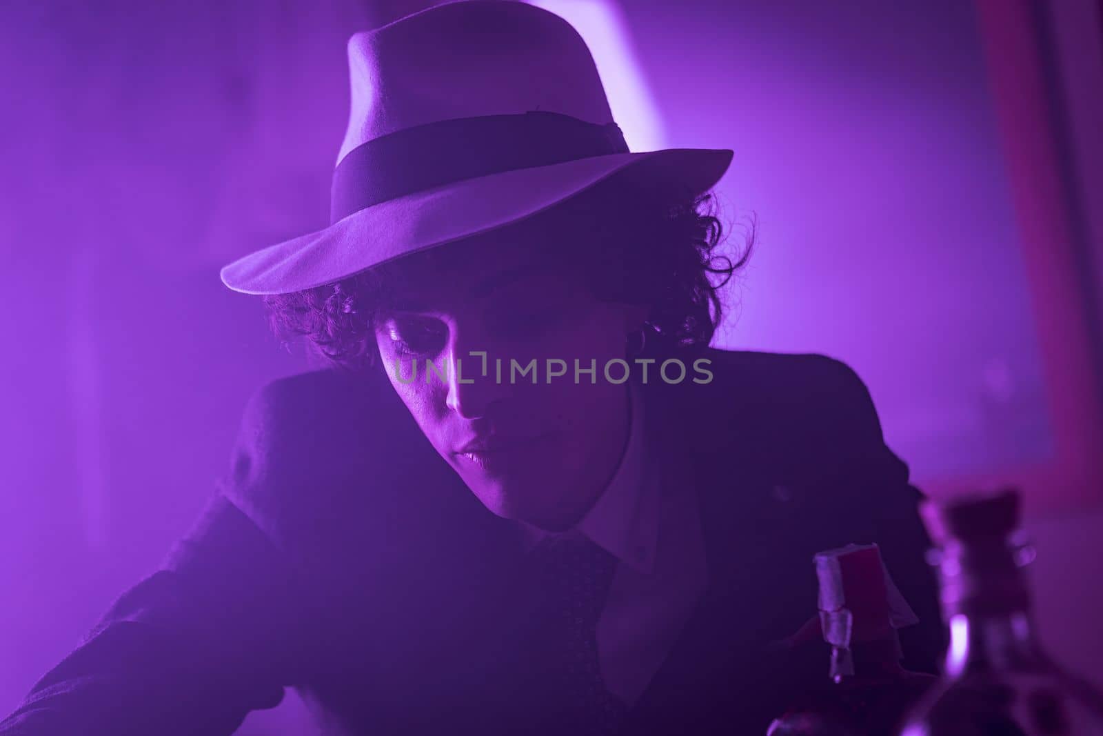 Young curly haired brunette man with hat and suit looks at the camera and smiles by pippocarlot
