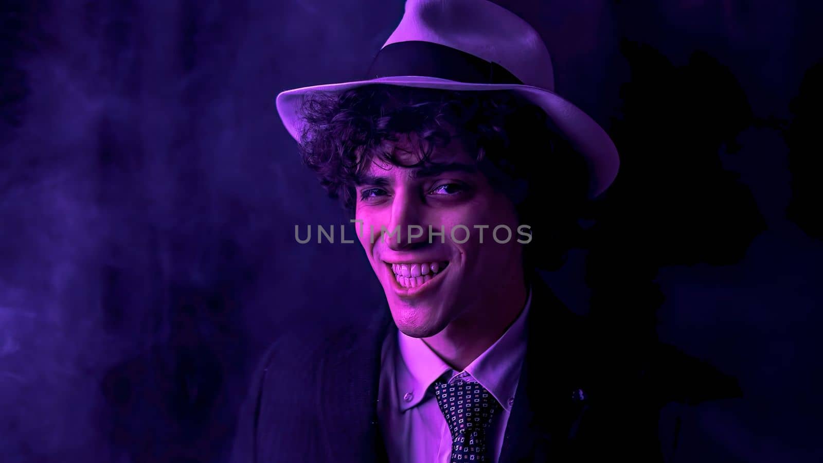 Young curly haired brunette man with hat and suit looks at the camera and smiles by pippocarlot