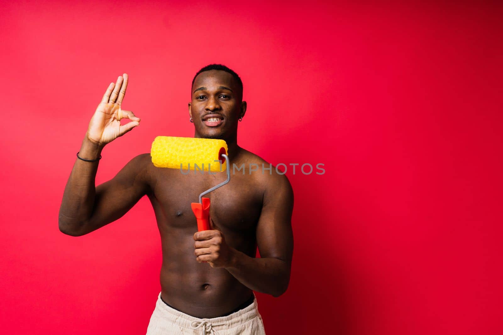 African painter focused on work holding professional roller to paint interior wall, studio.