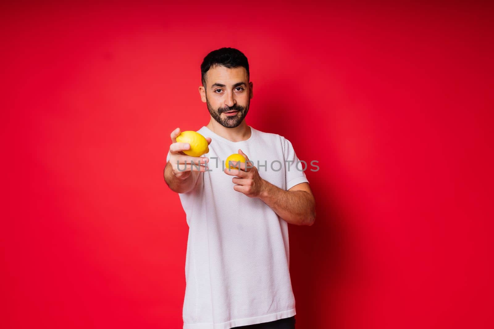 Portrait of young bearded man holding lemons in both hands on isolated red background by Zelenin