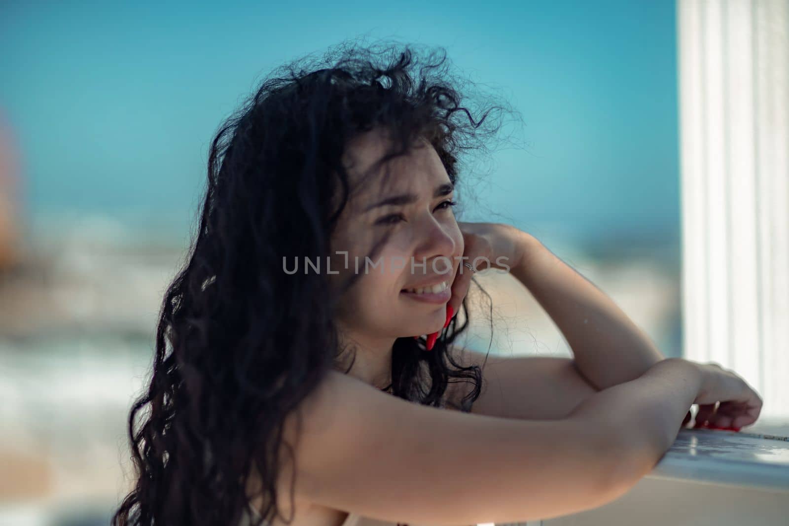 Sea woman rest. Portrait of a woman with long curly black hair in a beige dress stands on a balcony against the backdrop of the sea. Tourist trip to the sea