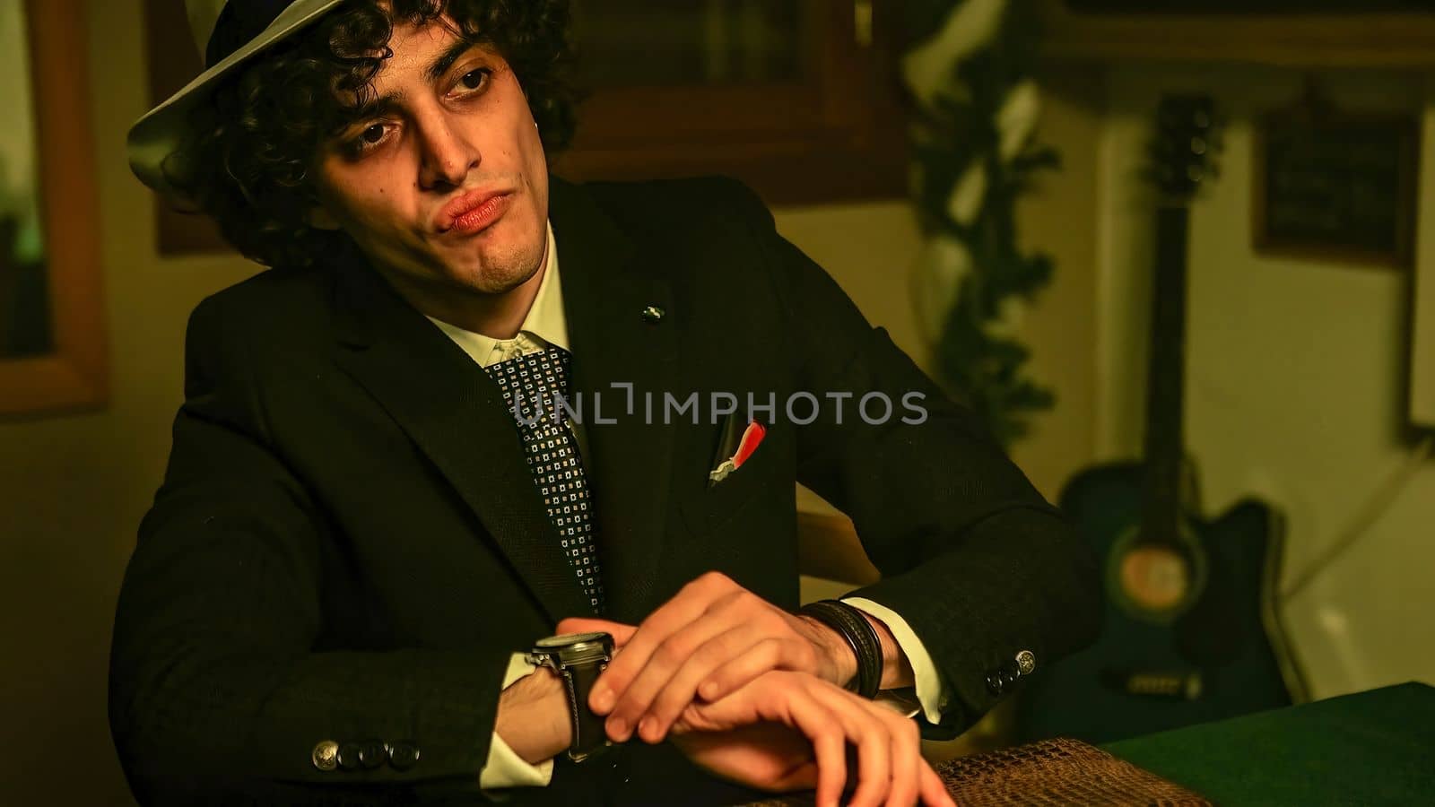 A man sitting in front of a briefcase on the table, checking the time on his wristwatch. He nods in affirmation, giving the impression that he is ready to close a deal.