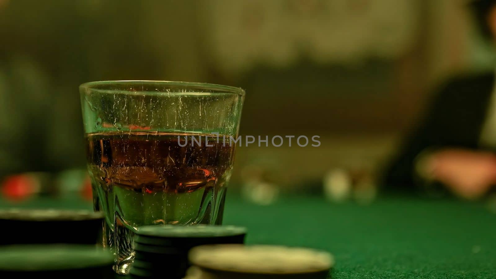 Man pours whiskey into a glass placed on a poker table surrounded by poker chips by pippocarlot