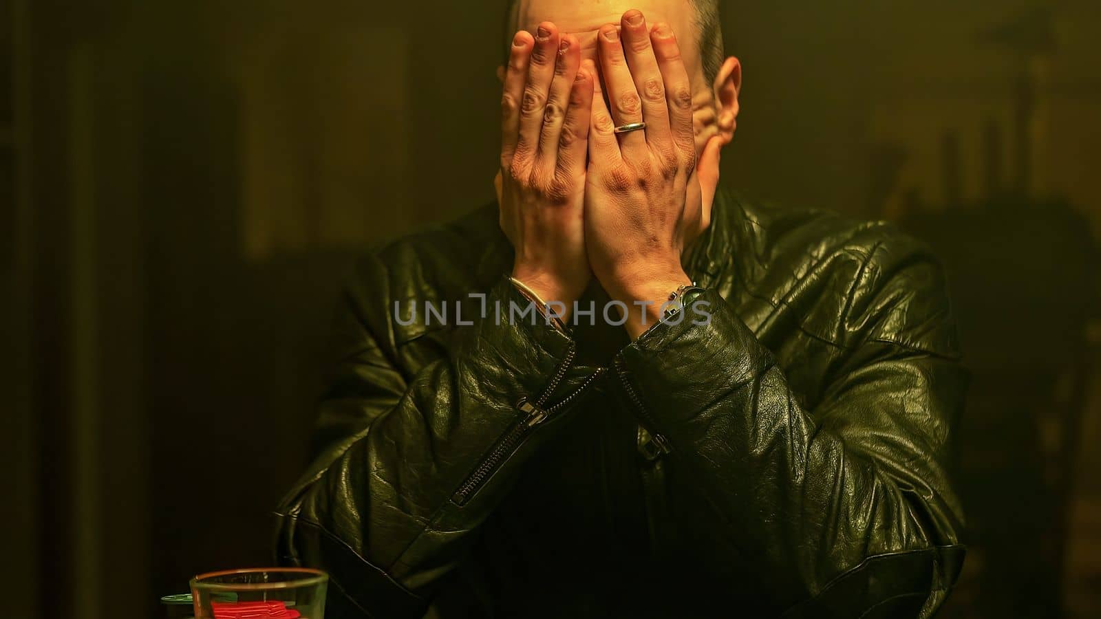 A poker player sits at a table with a look of fear on his face, as he contemplate the all-in bet in front of him while sipping whiskey. Sense of uncertainty and tension.