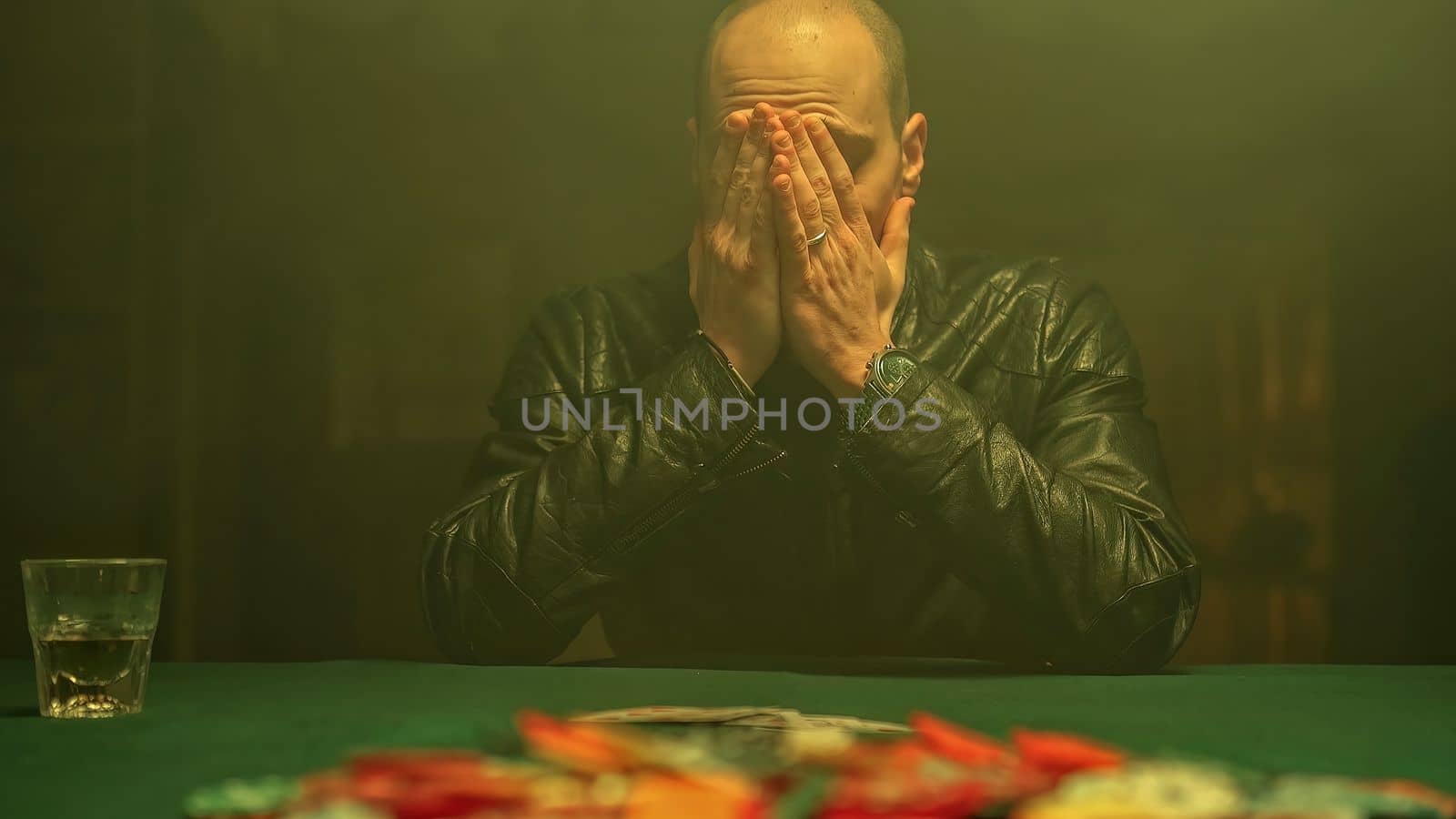 An excited poker player wins the game, reveals his cards while sipping whiskey and takes all the poker chips scattered on the table. Winning in gambling.