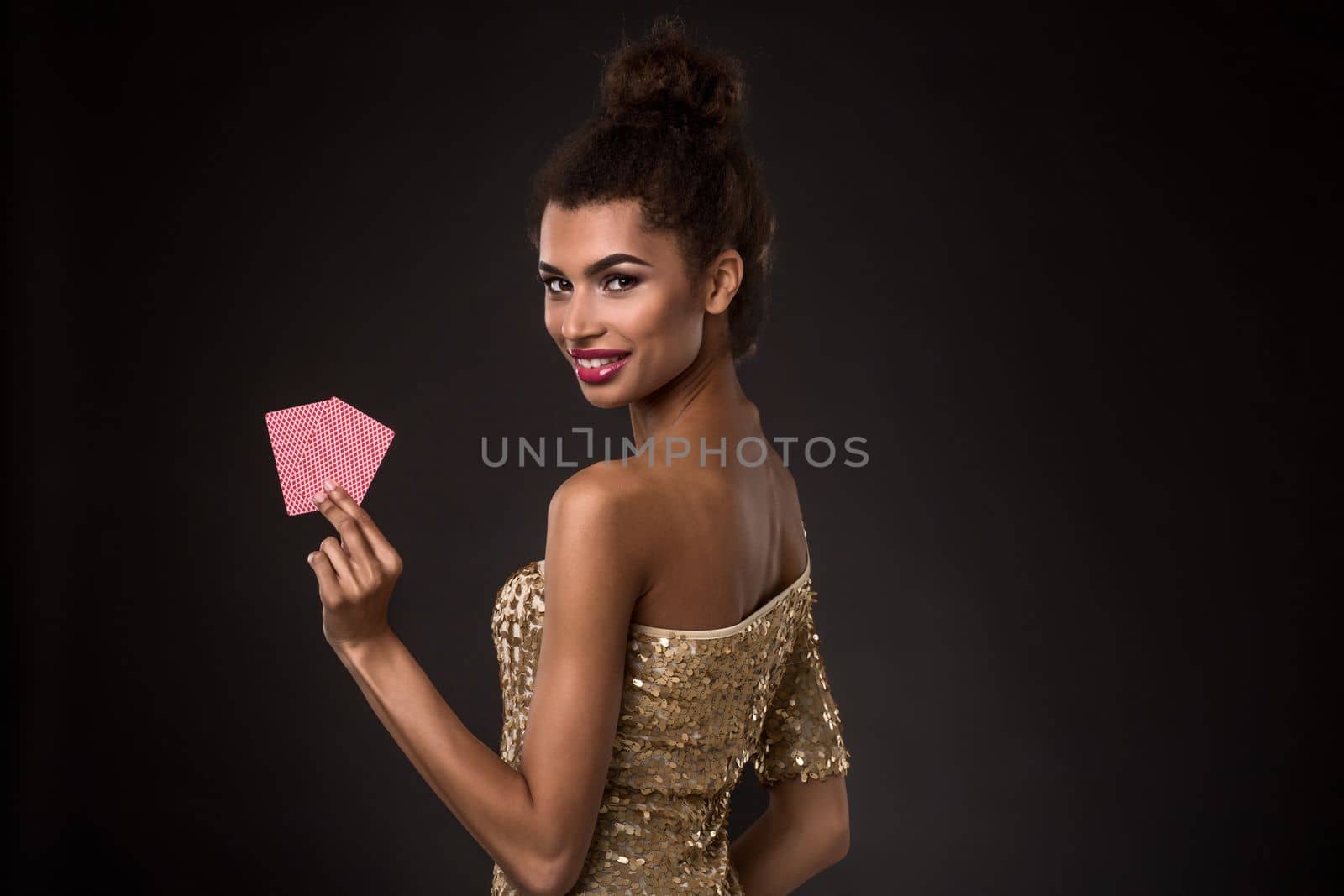 Woman winning - Young woman in a classy gold dress holding two cards, a poker of aces card combination. Studio shot on black background. A young woman stands with her back