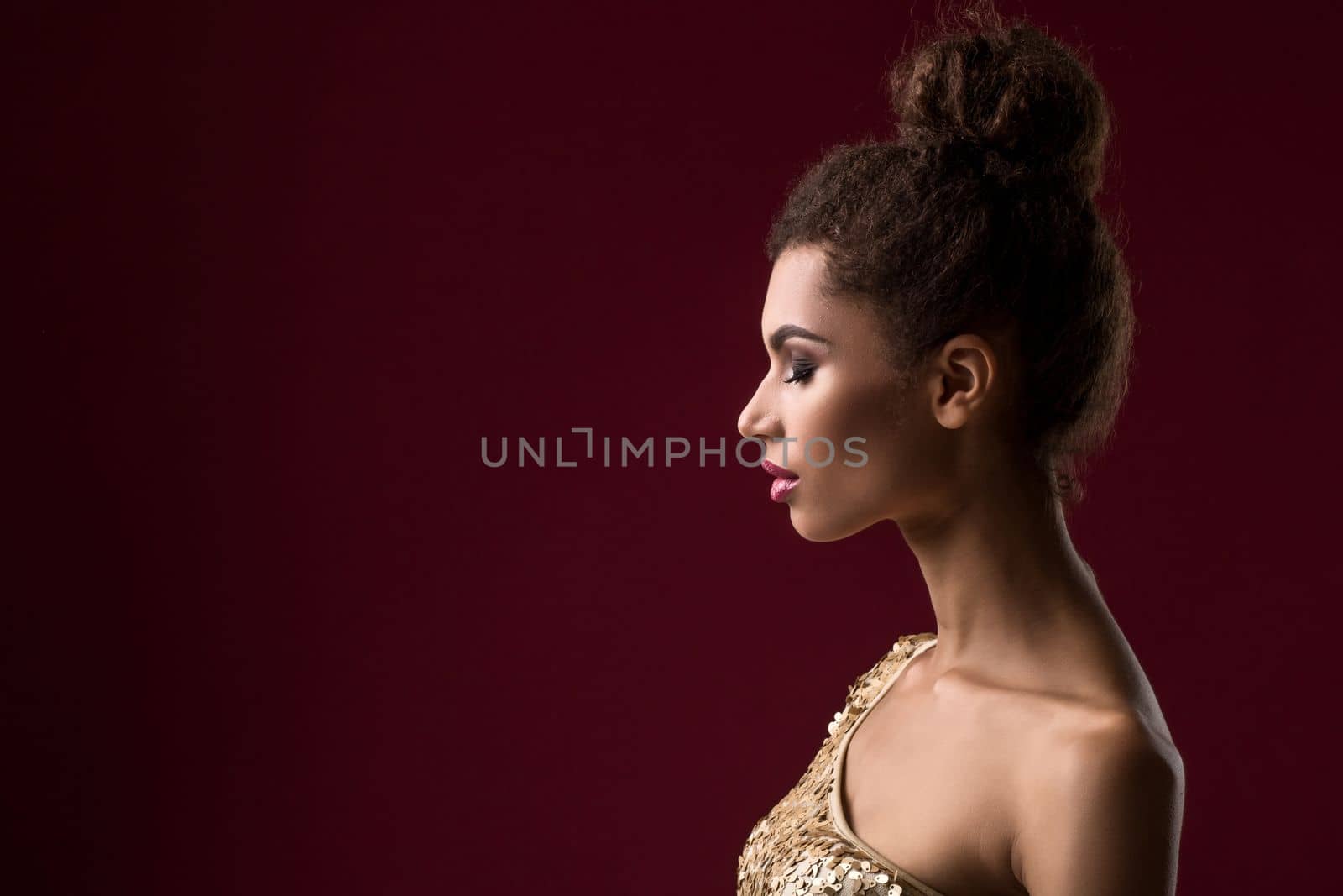 Fashion young African woman with make-up, in sexy gold dress. Model on a claret background in the studio. A woman is half a turn