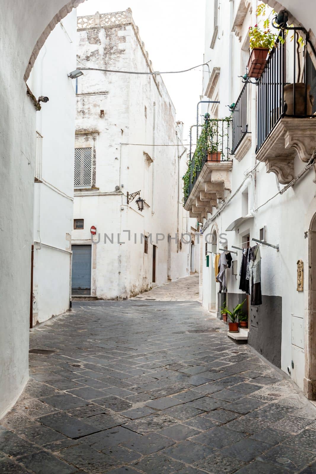 View from an archway on the empty streets of old town Martina Franca with a charming houses painted in white among greenery. Wonderful day in a tourist town, Apulia, Southern Italy.