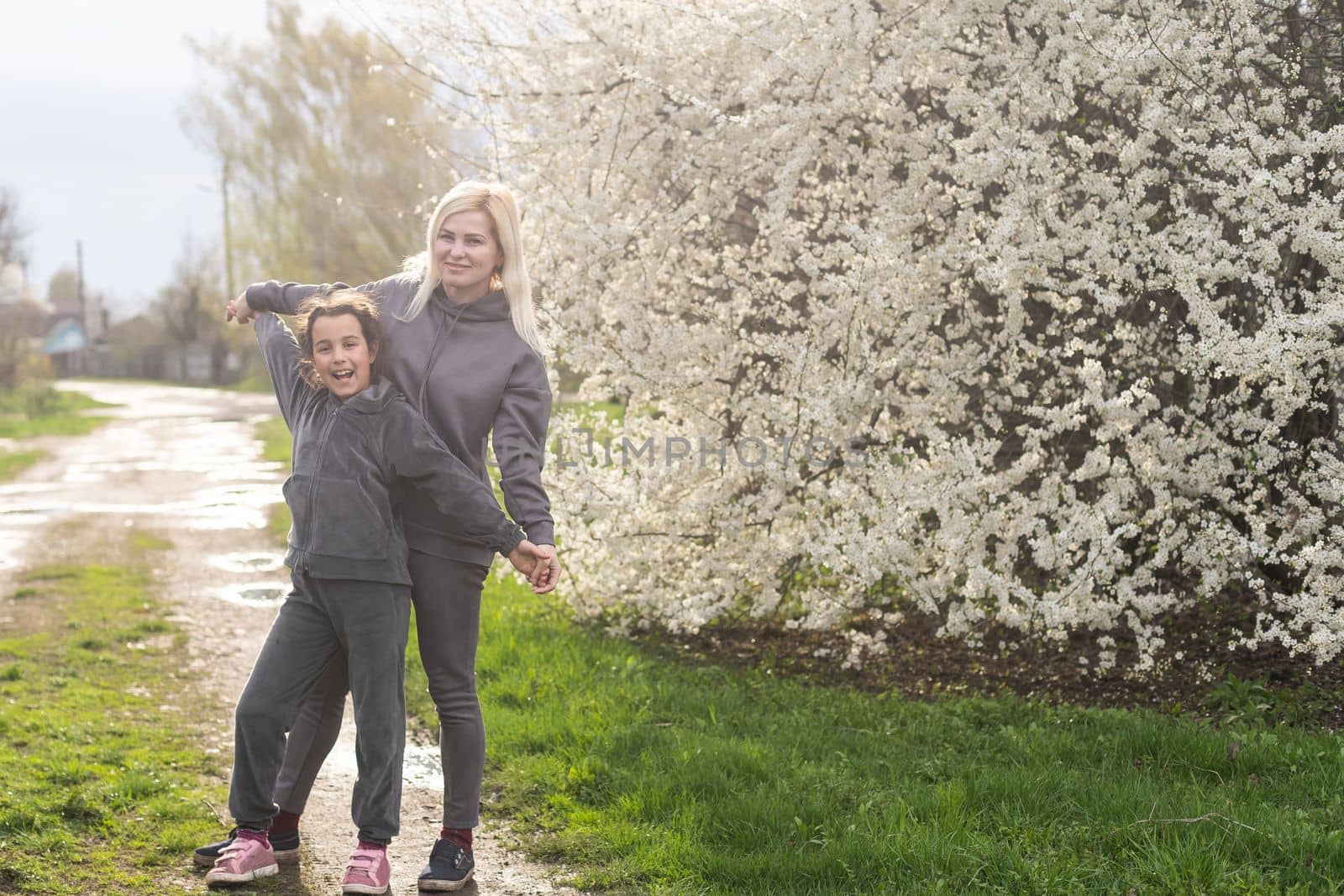 Woman walking with daughter in blooming spring garden exploring flowering tree. Family admires nature