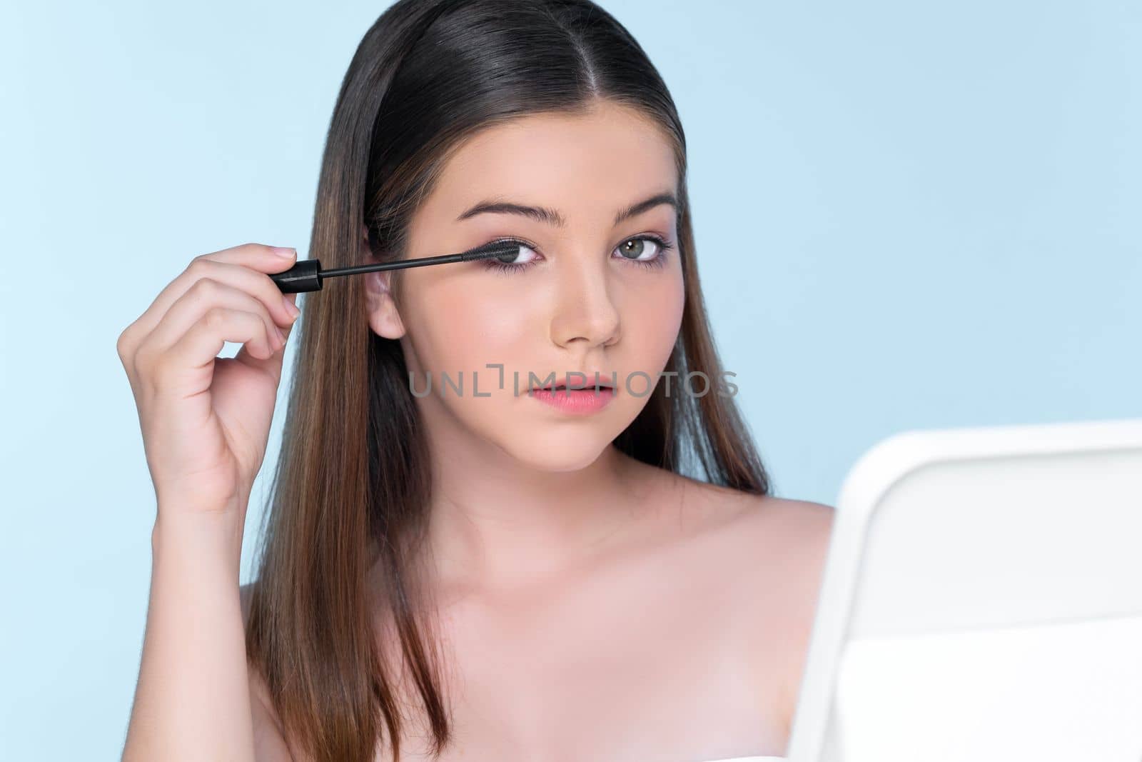 Closeup portrait of young charming applying makeup eyeshadow on her face with brush, mascara with flawless smooth skin for beauty concept.