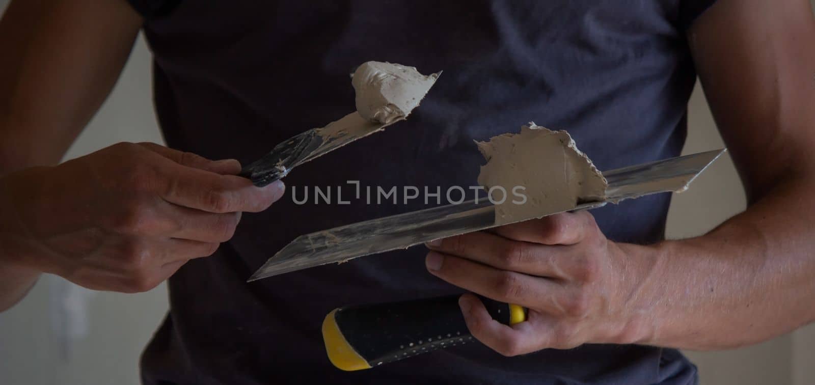 A man holds a spatula with putty in his hands. Selective focus. construction