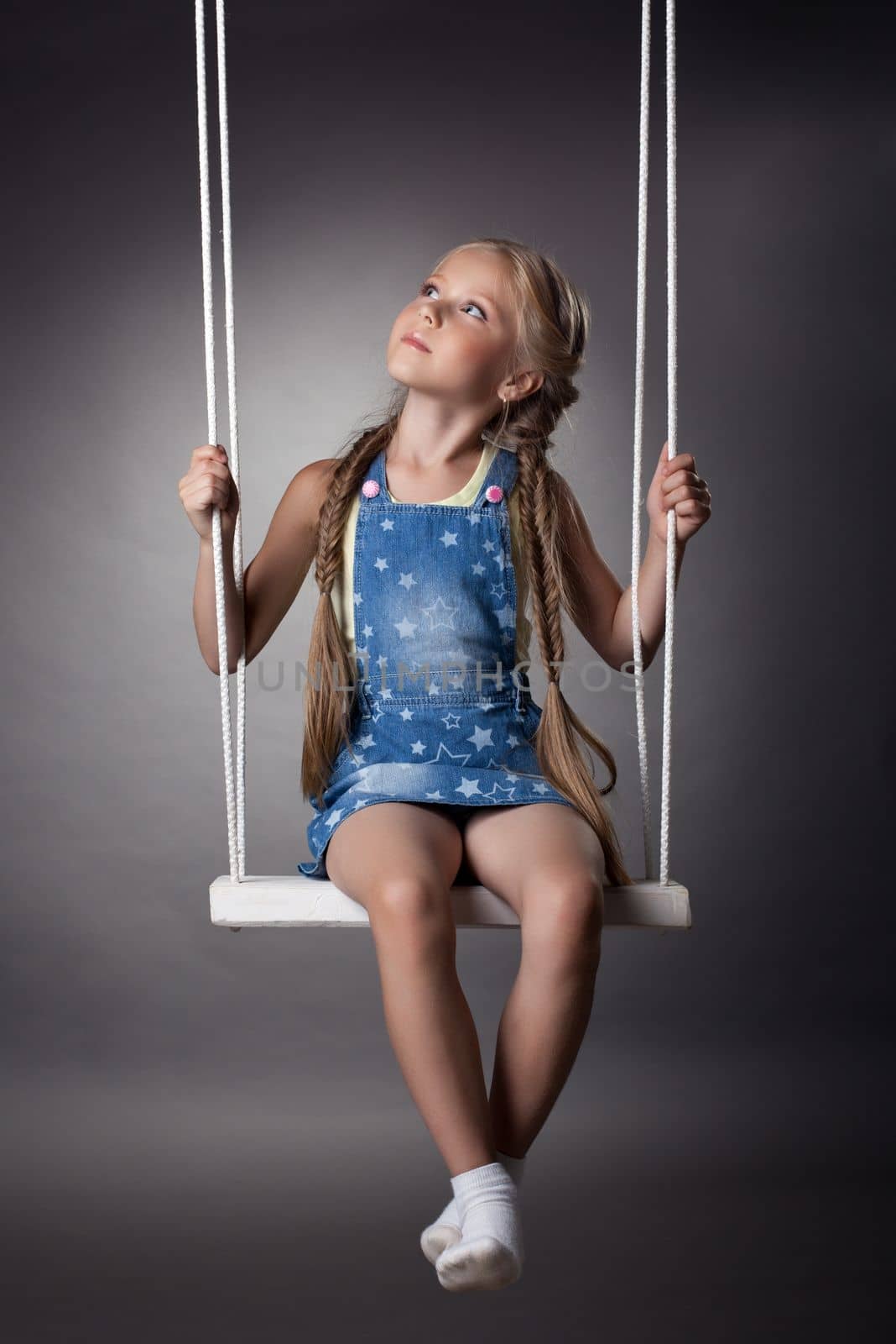 Studio portrait of beautiful blonde girl on swing