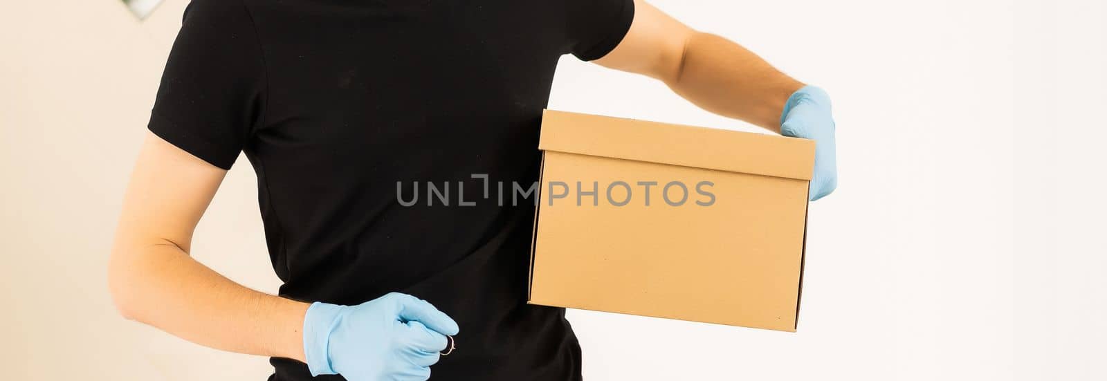 delivery man holding package to deliver. Courier hand holding brown box isolated on grey background. Detail of delivery man carrying cardboard parcel with label with copy space