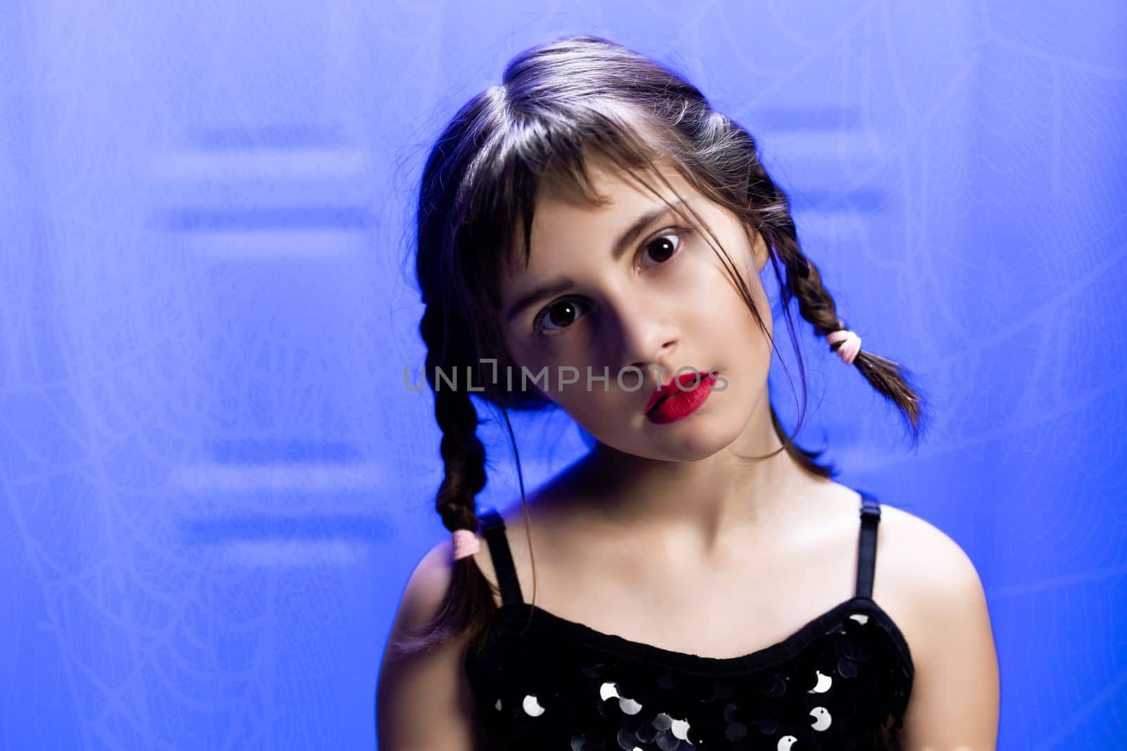Portrait of a beautiful girl in a black dress. A young girl is looks at the camera at home. Vampire girl in black medieval dress. Color background. Halloween costume