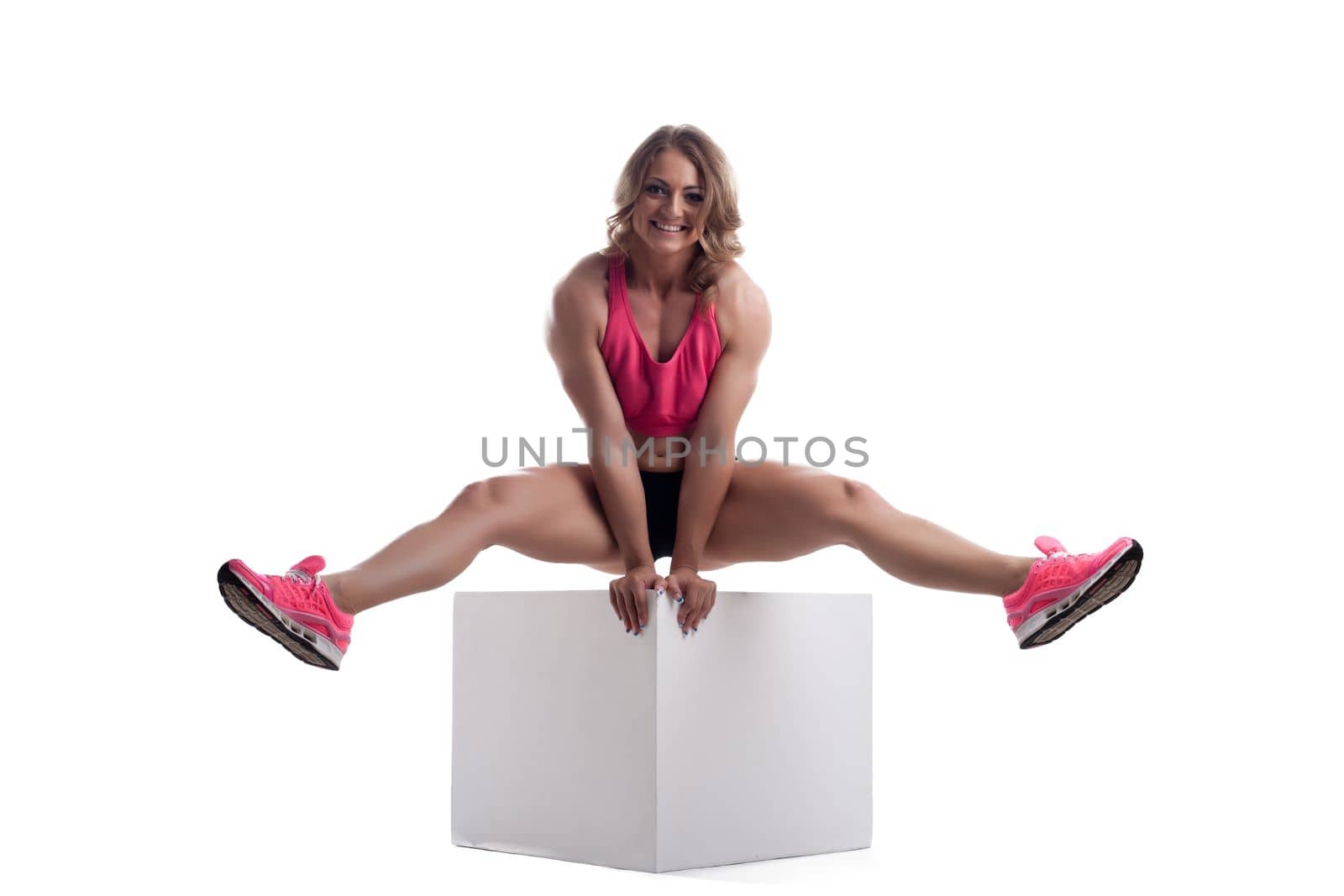 Happy athletic woman with perfect body sit on cube isolated