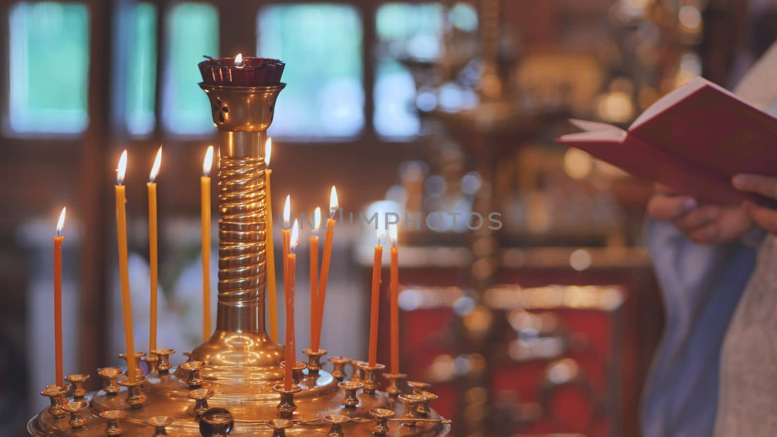 Burning candles against the background of the Priest reading the Bible at the service