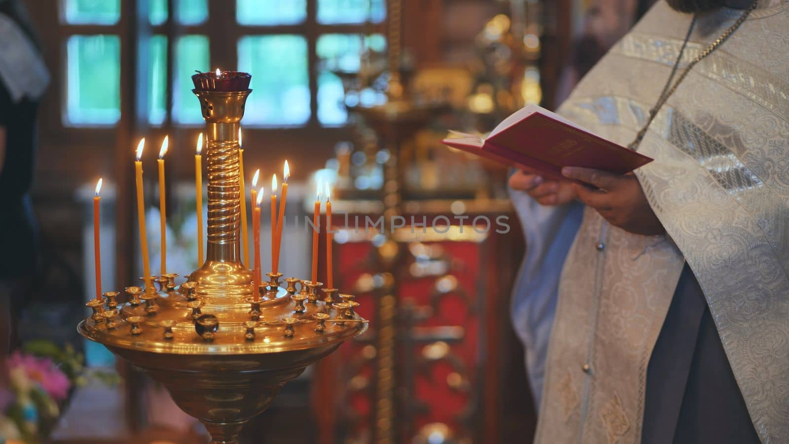 Burning candles against the background of the Priest reading the Bible at the service