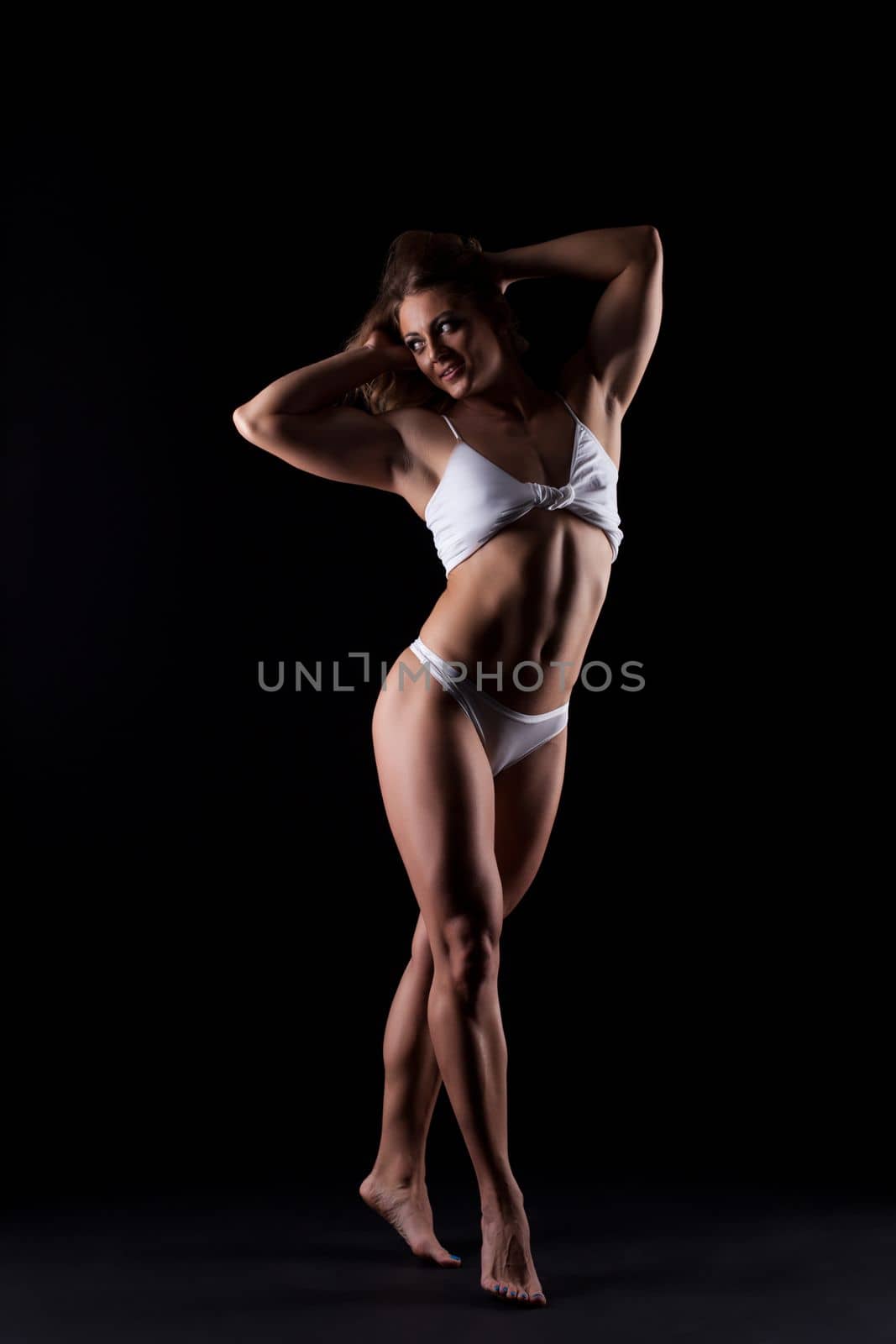 Athletic young woman in white panties posing in dark