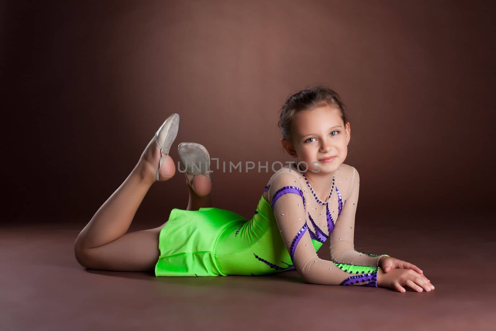 Young teen girl in green gymnast costume posing on brown background