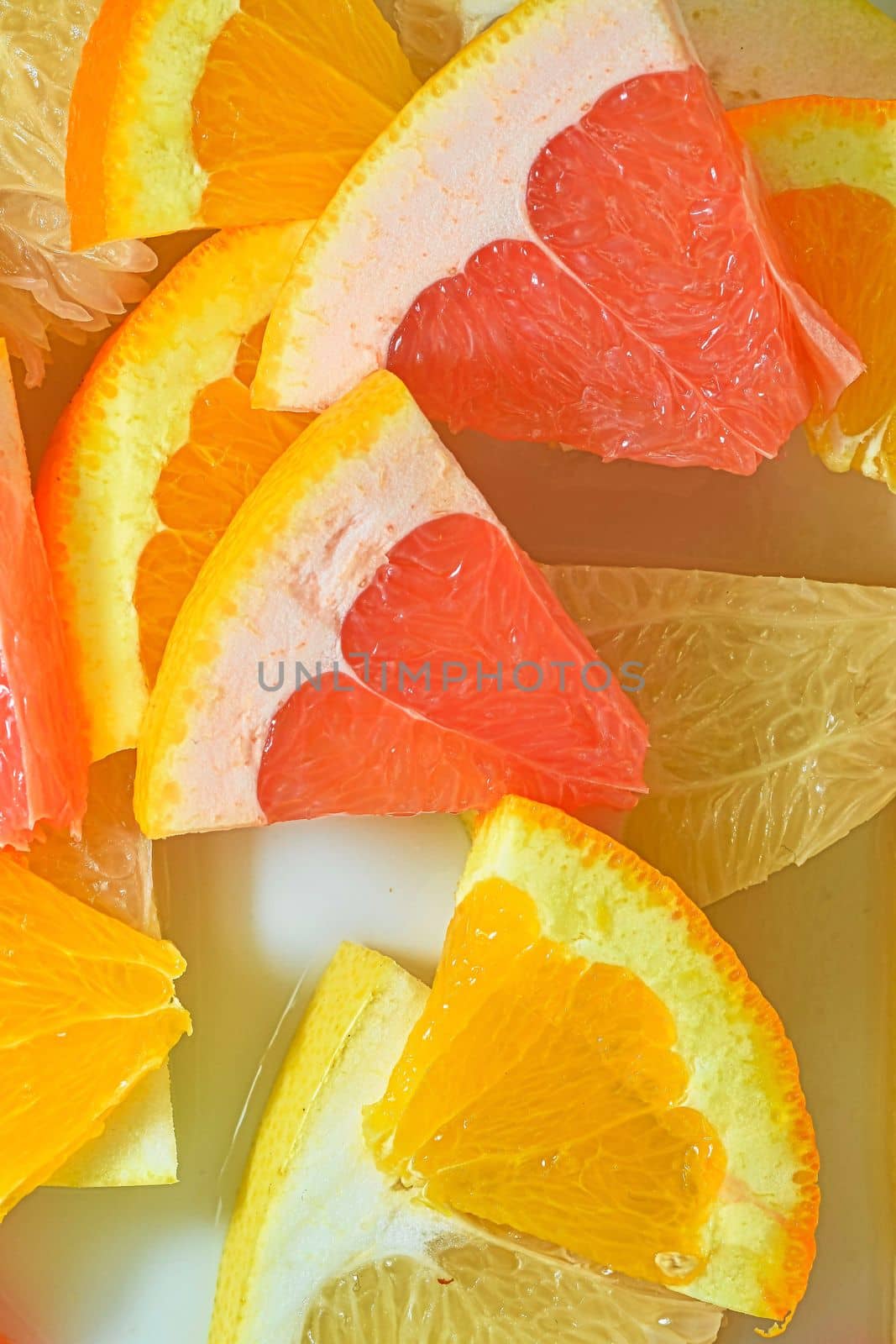 Slices of grapefruit, orange and pomelo in water on white background. Pieces of grapefruit, orange fruit and honey pomelo in liquid with bubbles. Slices of grapefruit, orange fruit and honey pomelo in water. Macro image of fruit in water. Vertical image. Top view, flat design by roman_nerud