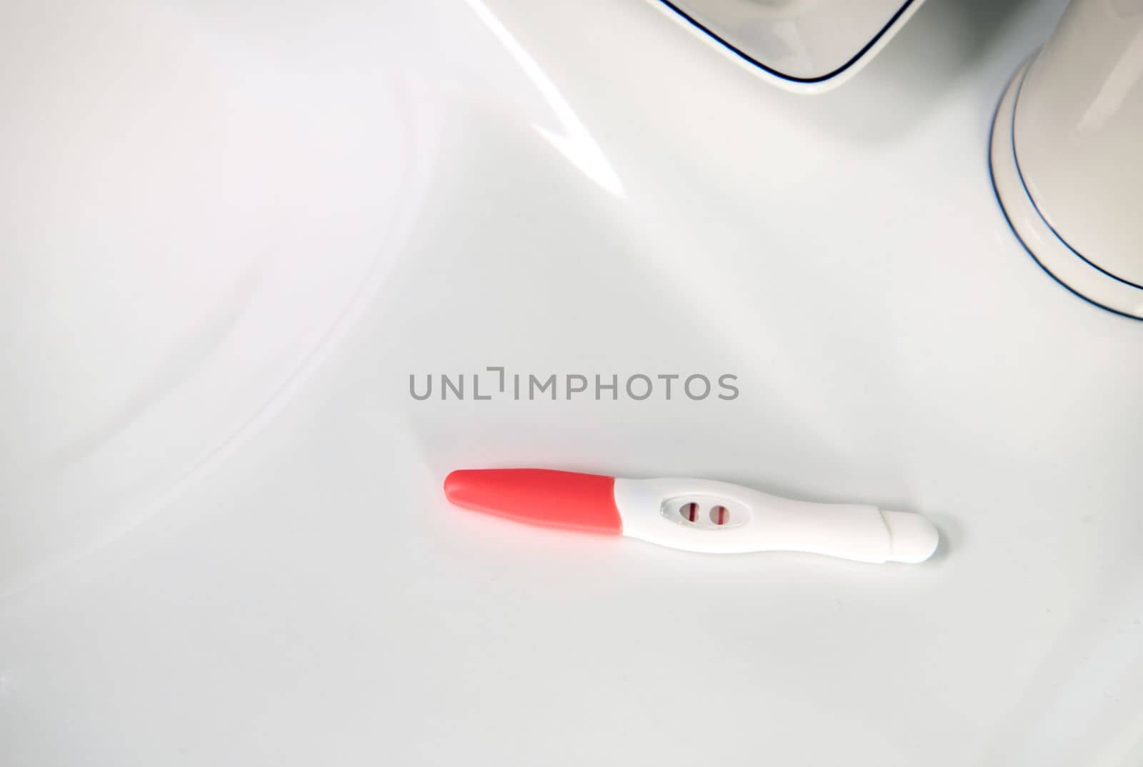 View from above. Selective focus on an inkjet pregnancy test in action with positive result on a white wahbasin in the home bathroom.