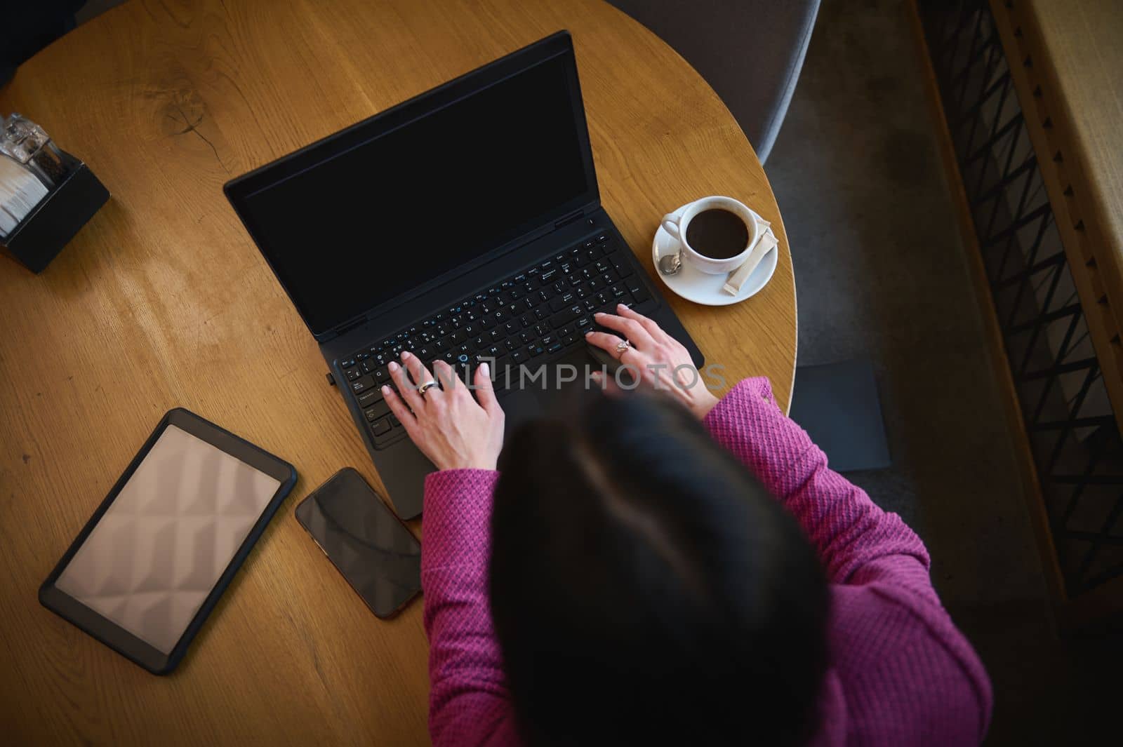 Overhead view Businesswoman typing text on laptop keyboard, working remotely on laptop with free space for your advertising text, sitting at a table with a cup of coffee, digital tablet and smartphone