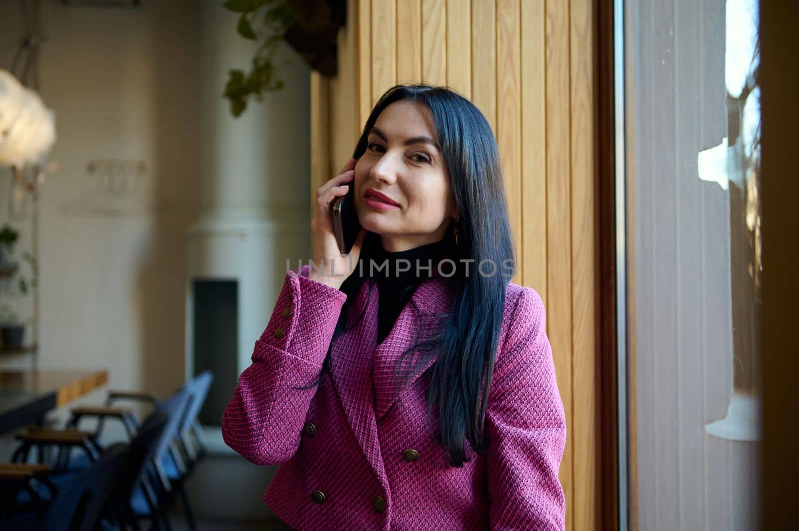 Caucasian confident stylish middle-aged brunette woman, businesswoman, chief executive, CEO, purposeful entrepreneur talking on mobile phone and looking at camera. People. Lifestyle. Business call