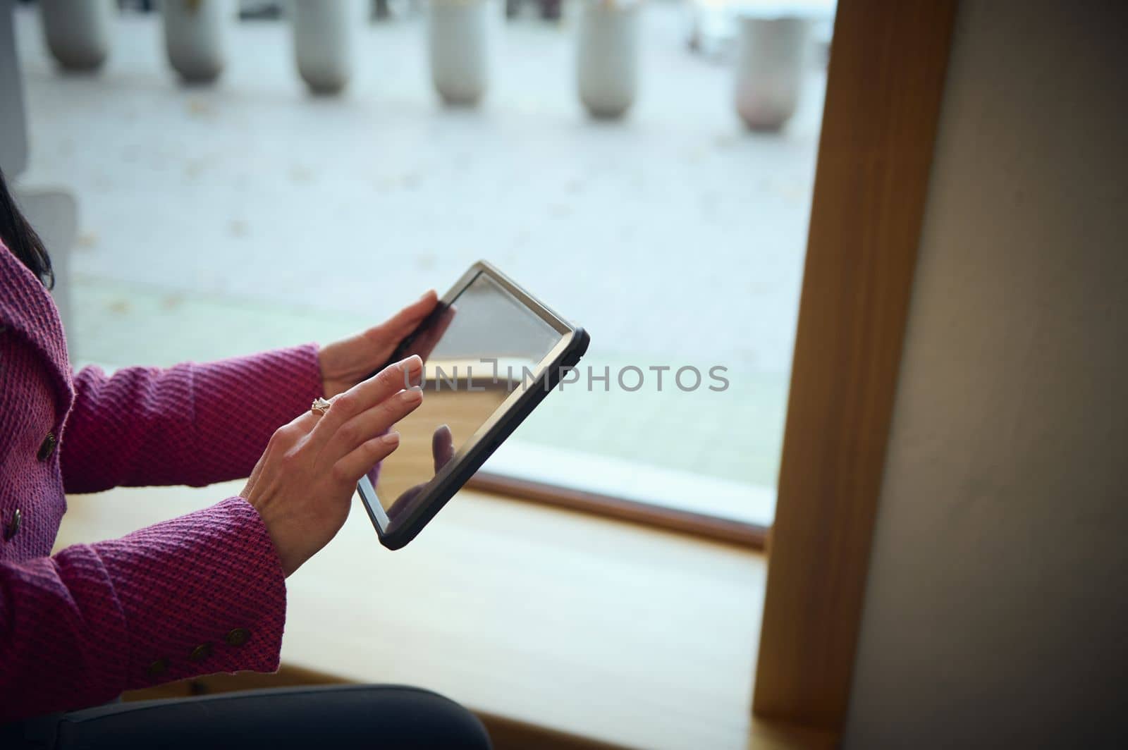 Close-up of the hands of a businesswoman working on digital tablet, sitting on the windowsill of her office by artgf