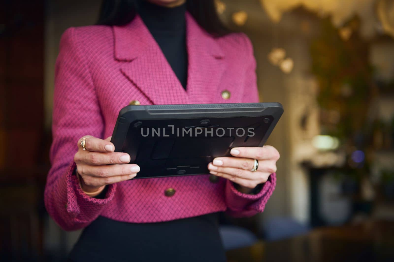 Details on digital tablet in the hands of a restaurateur, businesswoman in bright purple casual wear, executive director or successful manager, CEO against blurred background of a restaurant interior