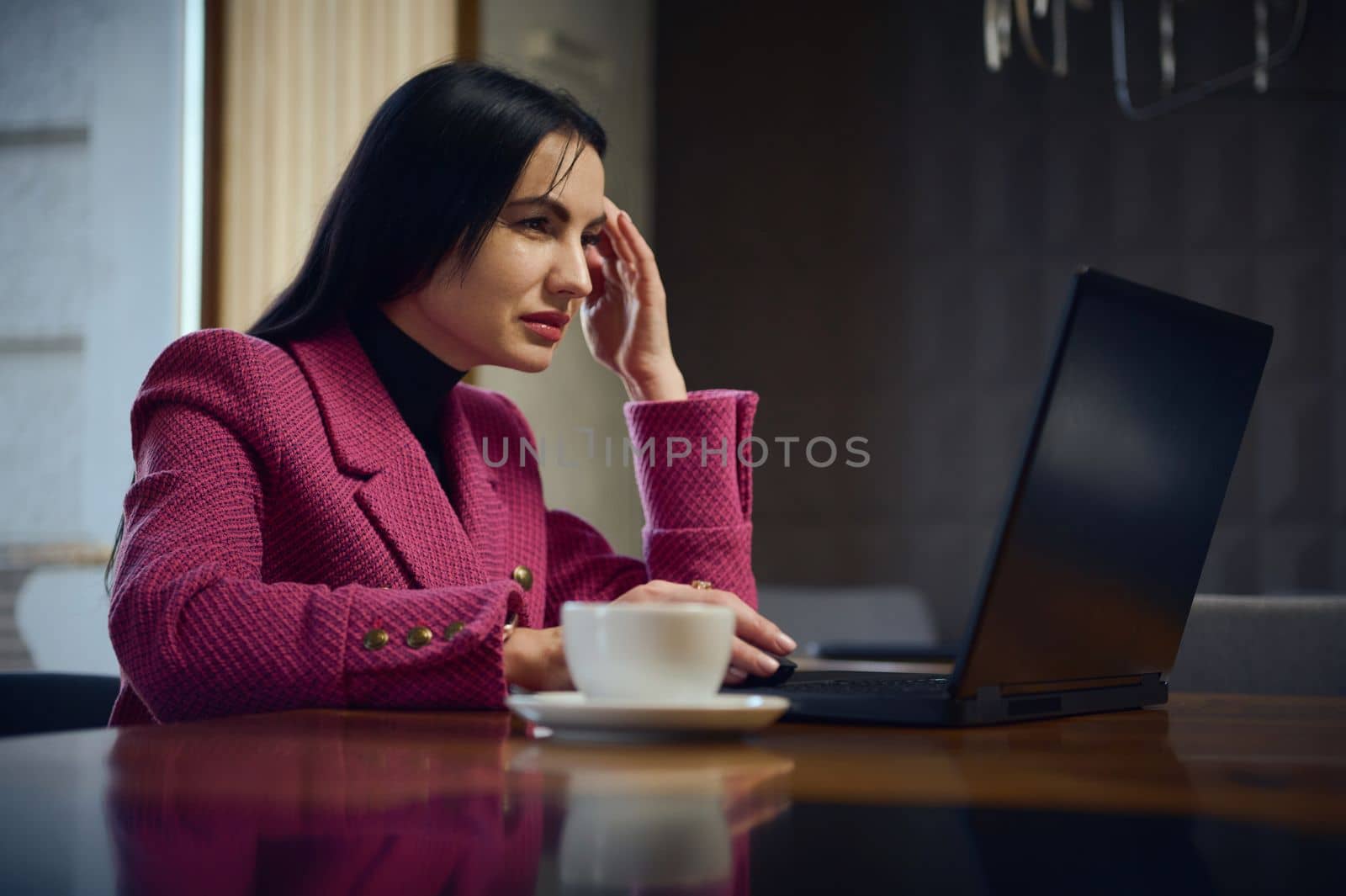 Confident Caucasian middle-aged business woman, entrepreneur, working remotely on laptop with a cup of coffee in cozy interior, planning new project, online chatting with business partners and clients