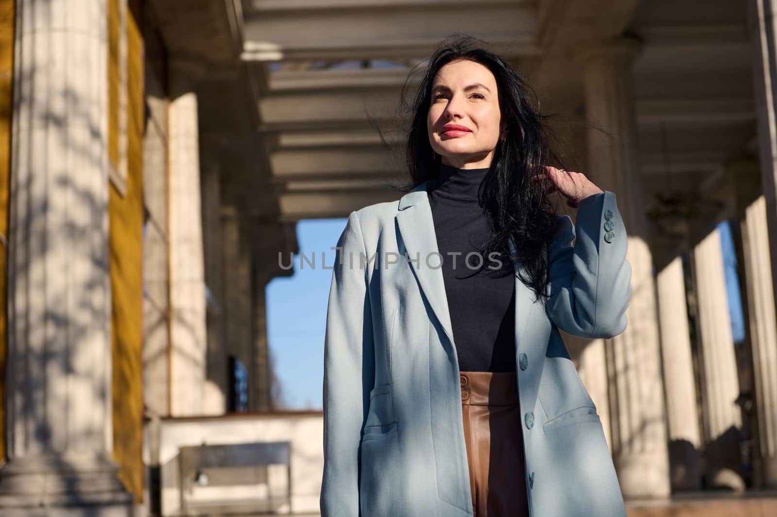 Portrait of beautiful self-confident elegant Caucasian woman 40-44 years old, walks down the street on beautiful sunny autumn day. The wind blowing beautiful woman's hair. Lifestyle People Urban life