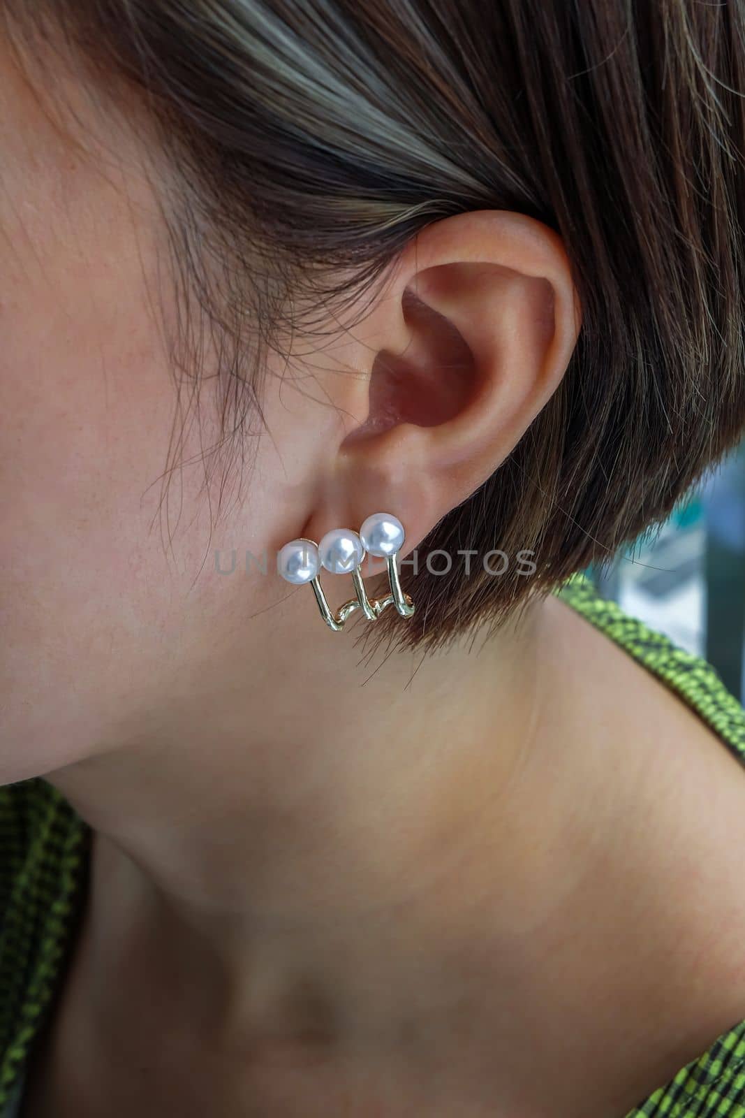 Detail of young woman wearing beautiful golden earring white pearl. Women accessories. Selective focus.