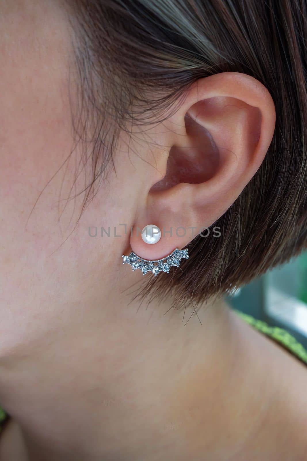Detail of young woman wearing beautiful silver earring white pearl and diamonds. Women accessories. Selective focus.