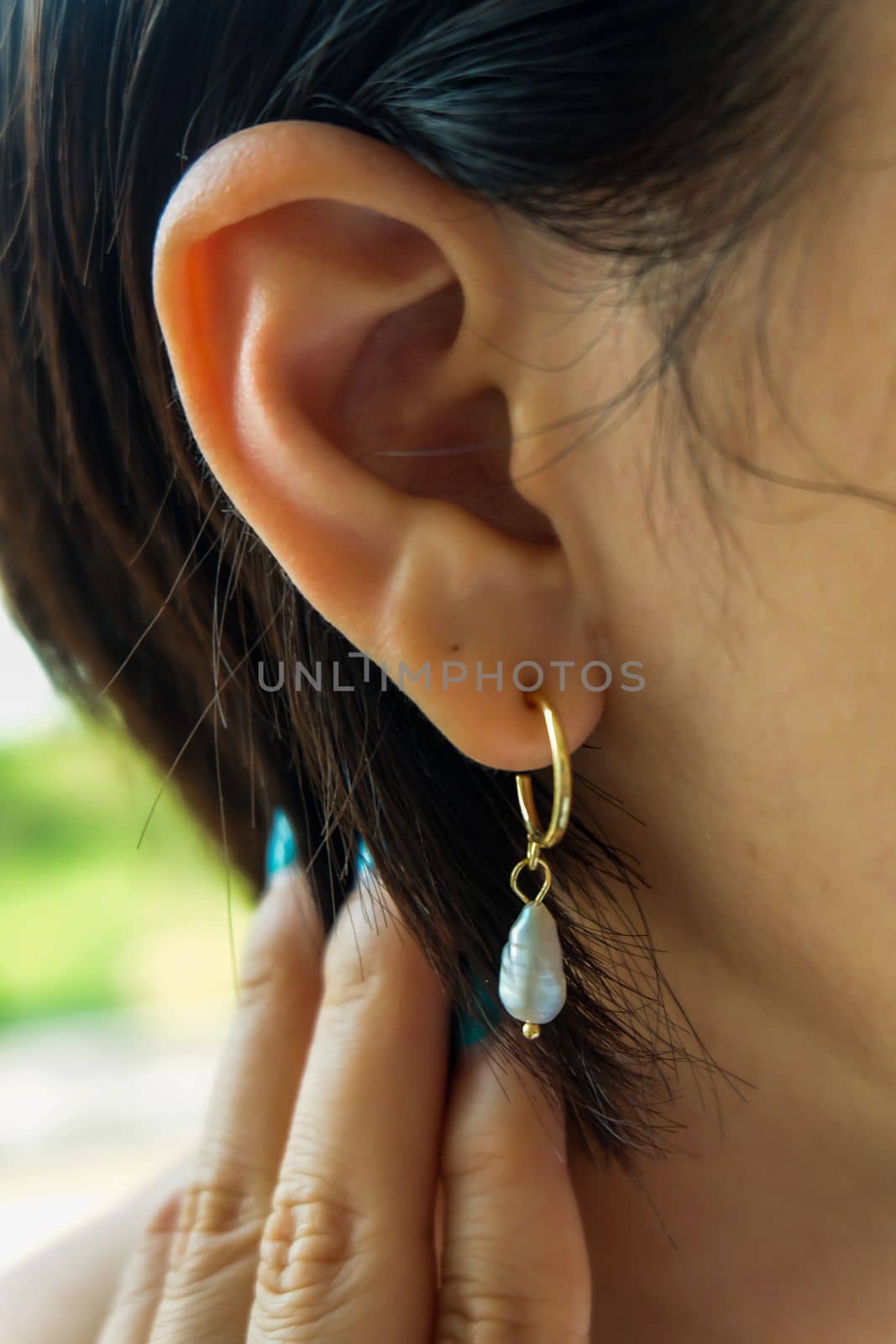 Detail of young woman wearing beautiful golden earring white pearl. Women accessories. Selective focus.